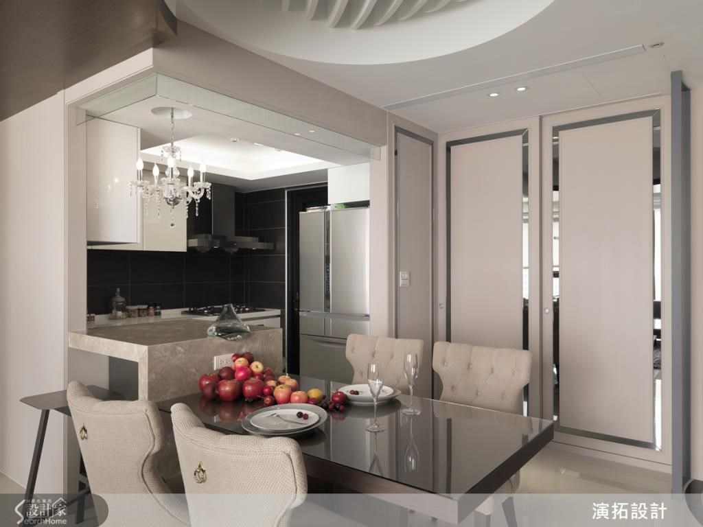 開放式餐廚空間將餐桌與吧檯做連結，滿足多人的宴客需求，並以小巧精緻的吊燈形成視覺亮點，旁邊牆面則配置依家具量身打造的餐廚櫃，整齊美觀。