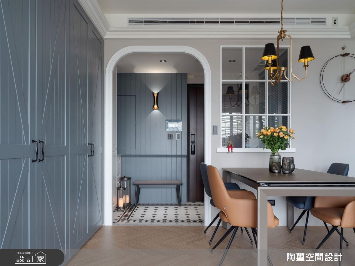 木作的拱型門框與格柵窗型相互平衡，使整體視覺更為柔和，打亮玄關、清透場域，成為玄關進入家中優雅的轉場。鐵件手把的莫藍迪藍穀倉門，是深度達60公分的大型落地收納儲物櫃，大型家電、家用備品、行李箱等都能輕易歸類，收納機能十分強大。