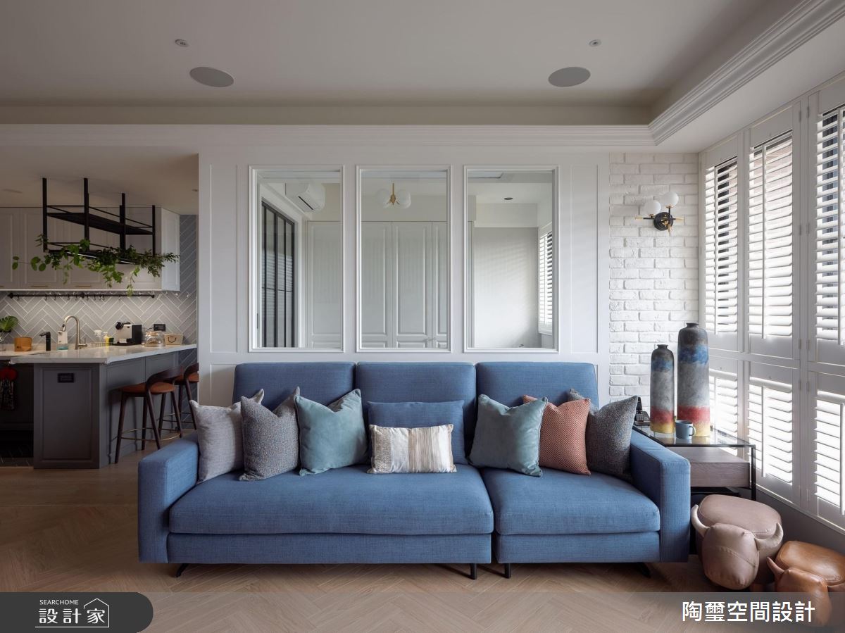 美式經典大片百葉窗，溫和地帶入美好的自然光源，文化石牆與清新的藍色布面訂製沙發，佐以一盞畫龍點睛的金屬壁燈，以及人字拼的超耐磨木地板，將美式風格居家的元素充分地運用在客廳公領域。