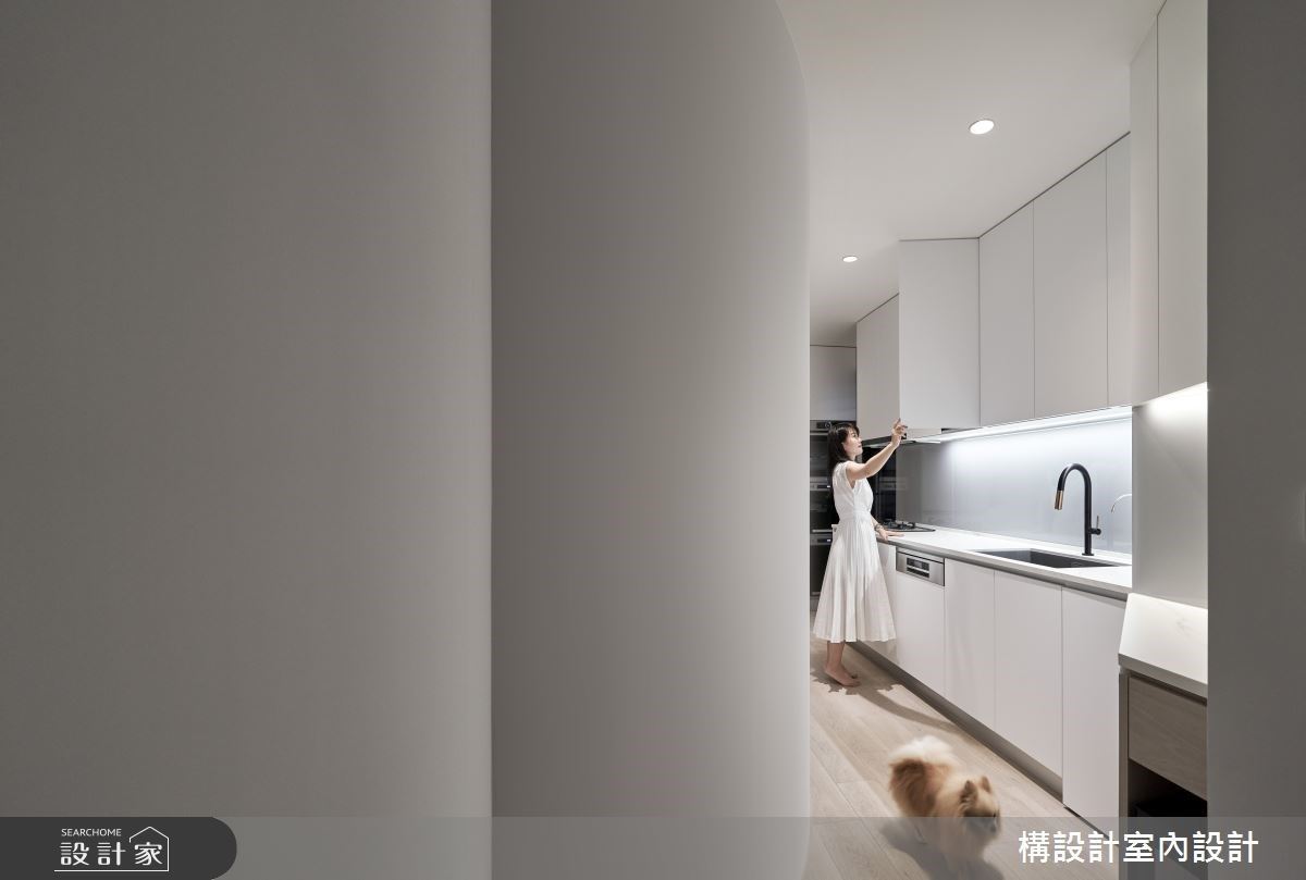 廚房利用弧形造型隱藏樑柱，將檯面、電器整合在一側，拉長廚房的工作區域，大尺度檯面化解原先格局的劣勢，成為極具特色的工作吧檯。